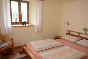 A bedroom with a bed, a chair, a window with curtains, and a nightstand. - "Am Teich" on the Sanderhof (Rathmannsdorf)