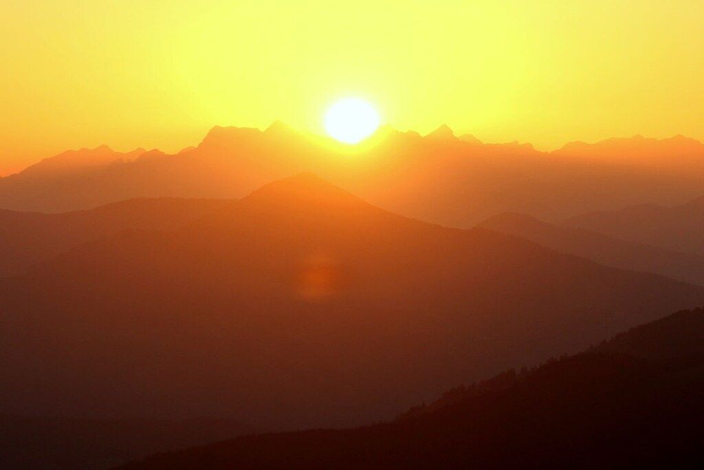 A mountain range with a sun setting or rising behind it.