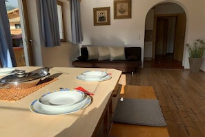 A dining area with a wooden table set for two, a sofa in the background, and a view of the kitchen through an archway. - Top 2 in the Alpin house (Uderns)