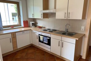 Una cuina compacta amb armaris blancs, forn integrat, rentapeus i finestra que ofereix llum natural.