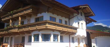 A traditional chalet with a balcony, a garage, and a mountain backdrop.