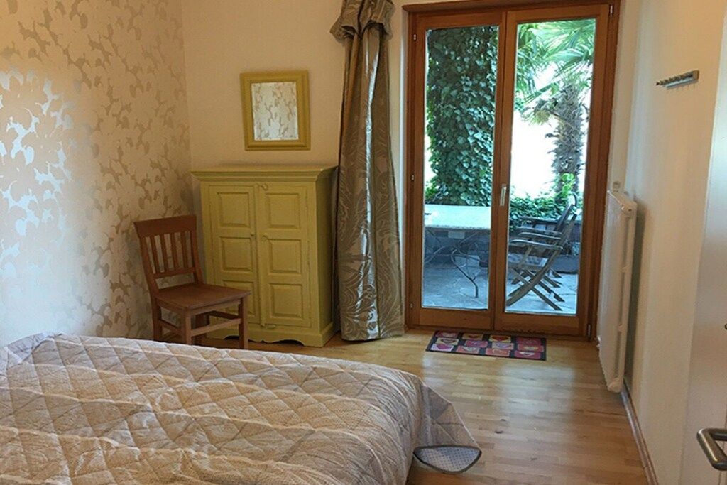 A bedroom with a bed, a wooden chair, a yellow cabinet, and a sliding glass door leading to an outdoor area.