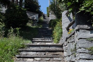 Un escalier en pierre menant au sommet d’une colline, entouré de verdure et bordé d’une rambarde métallique d’un côté.
