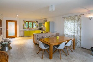Un coin repas avec une table et des chaises en bois, un canapé et, au fond, une cuisine.