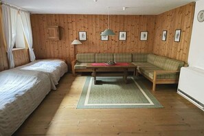 A room with wooden panel walls, a green sofa, a wooden table, and two single beds. - Holiday home in Nussdorf with swimming pool (Nussdorf)
