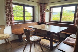 A dining area with a wooden table, chairs, benches, and large windows with curtains. - Holiday home in Nussdorf with swimming pool (Nussdorf)