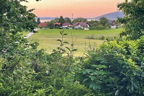 Paisagem rural com casas, um campo e uma colina ao fundo.