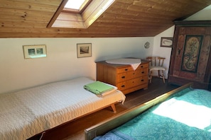 Quarto com claraboia, cama, cômoda e cadeira.