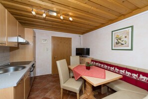 A compact kitchen with a wooden ceiling, a sink, a stove, and a dining area with a table and chairs. - Lady's Mantle - Apartment (St. Johann Pongau)