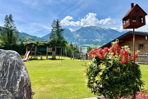 A mountain view with a wooden cabin, a playground, and a large rock in a garden. - Lady's Mantle - Apartment (St. Johann Pongau)