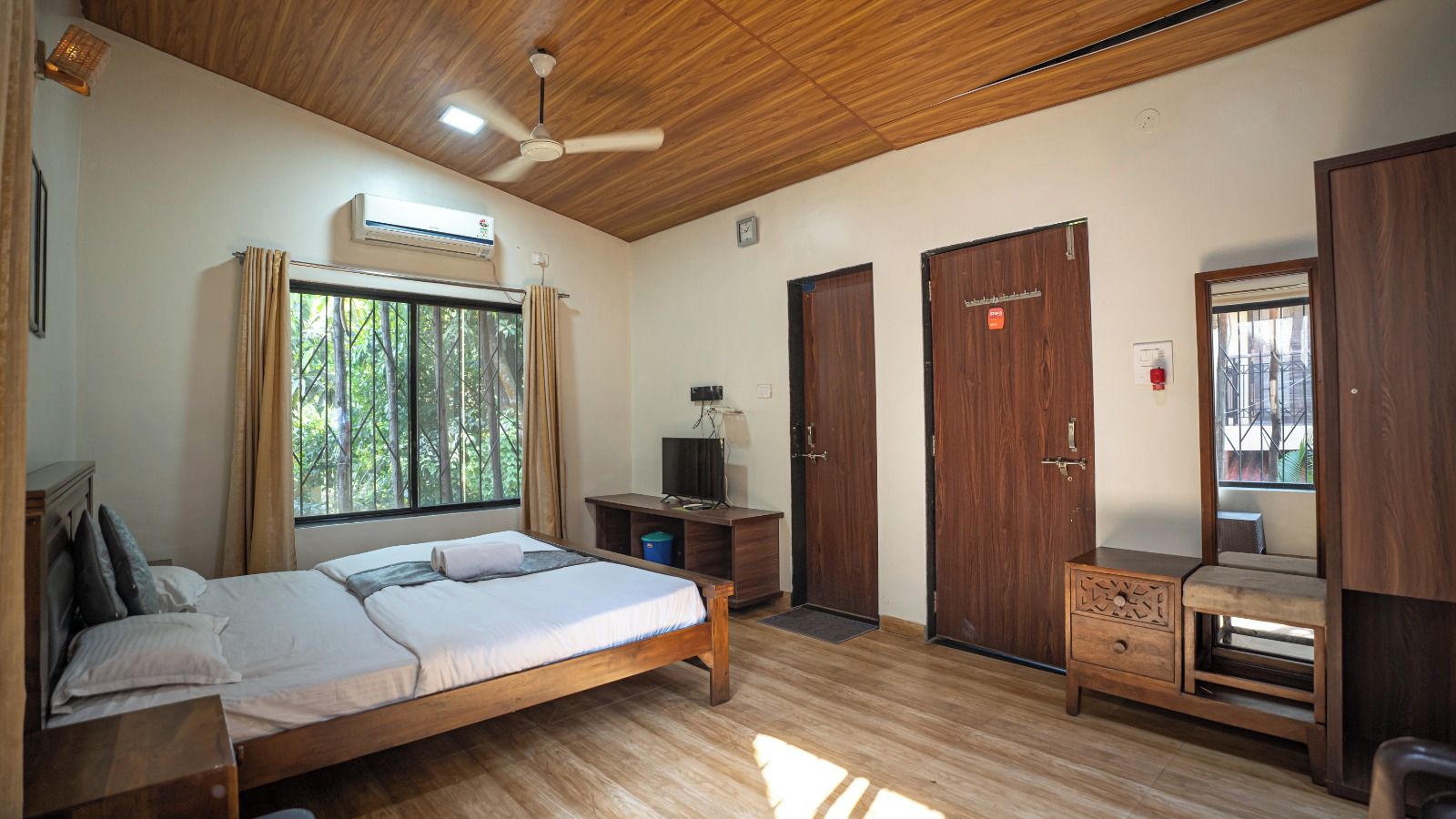 Un dormitorio con techo de madera, una cama, un escritorio, un televisor y dos puertas.