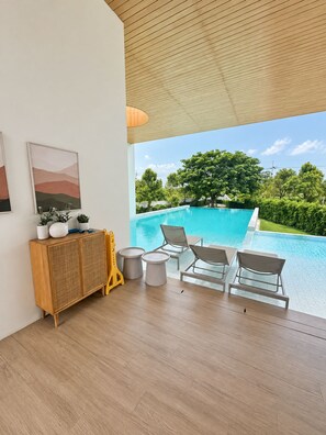 A modern room with a wooden ceiling, a pool view, a rattan cabinet, and a painting on the wall.