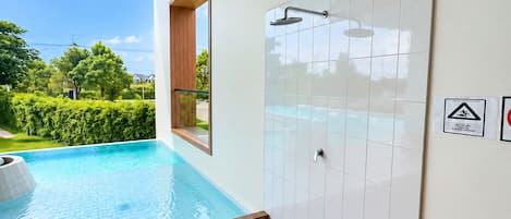 Ett modernt badrum med dusch, en liten pool och utsikt över en trädgård.