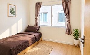 A bedroom with a bed, a window with curtains, a framed picture on the wall, and a potted plant.