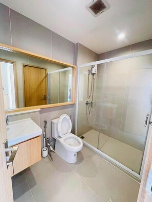 Un baño moderno con inodoro, lavamanos y ducha con mampara de vidrio.