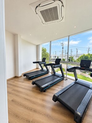 A gym with treadmills, a laptop on one, and a view of the outside.