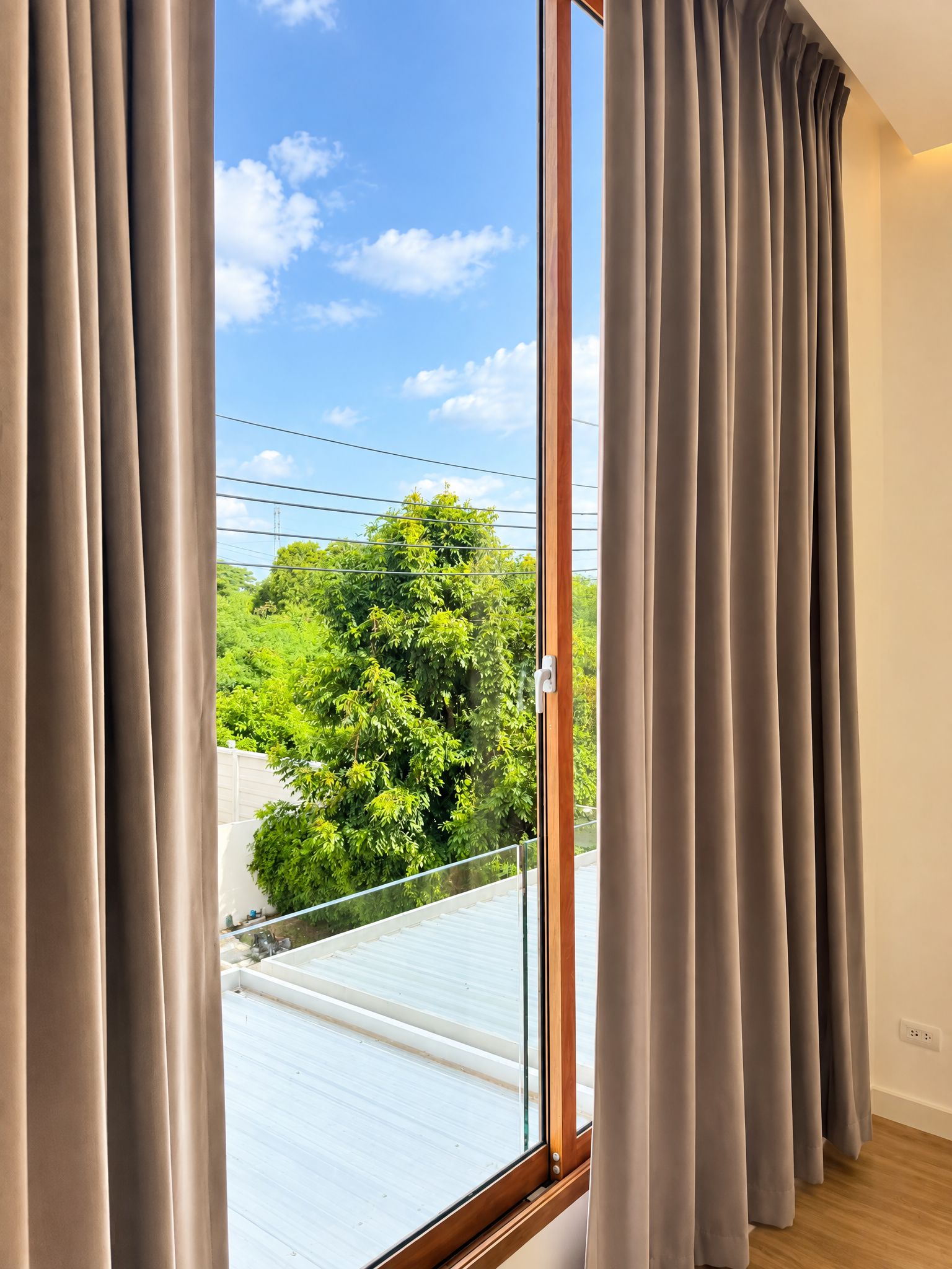 A room with a large window, curtains, and a view of greenery outside.