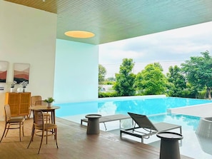 Un área interior de piscina moderna con suelo de madera, sillas de descanso y una mesa de comedor.