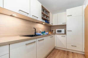 Cuina moderna amb armaris blancs, microones i un rentaplat.