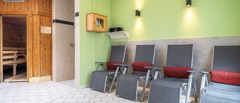 A sauna room with wooden walls, a bench, and four reclining chairs with red cushions.