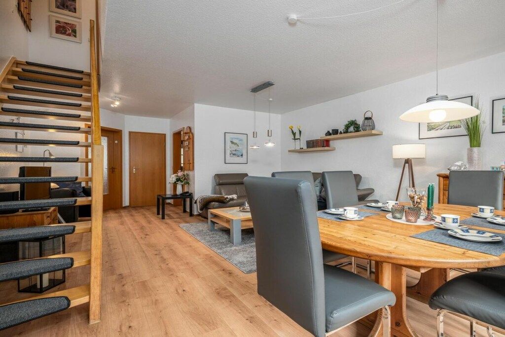 Un salon moderne avec un escalier en bois, un coin repas avec une table et des chaises en bois, et un ensemble de canapés.