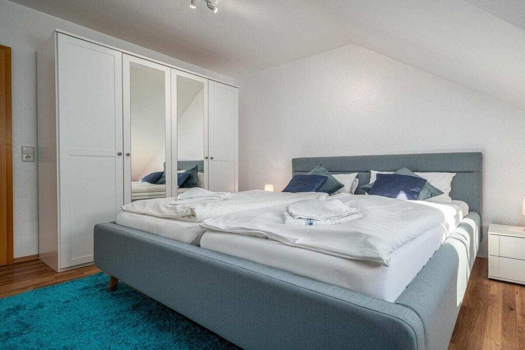A bedroom with a bed, a wardrobe, a nightstand, and a blue rug.