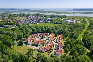 Ein Luftbild eines Wohngebiets mit Häusern, Grünflächen und einem Gewässer im Hintergrund.