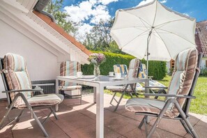 Eine Terrasse im Freien mit Tisch und Stühlen, einem großen Sonnenschirm und einer Blumenvase.