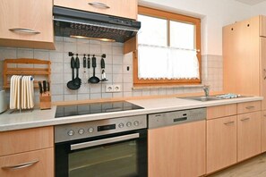 A modern kitchen with a built-in oven, a dishwasher, and a window with a curtain. - 5c/T5 Holiday Park "Freesenbruch" (Zingst (Ostseeheilbad))