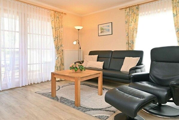 A living room with a sofa, a black leather chair, a wooden coffee table, and a floor lamp. - 5c/T5 Holiday Park "Freesenbruch" (Zingst (Ostseeheilbad))