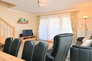 A living room with a TV, leather chairs, a sofa, a staircase, and a window with curtains. - 5c/T5 Holiday Park "Freesenbruch" (Zingst (Ostseeheilbad))
