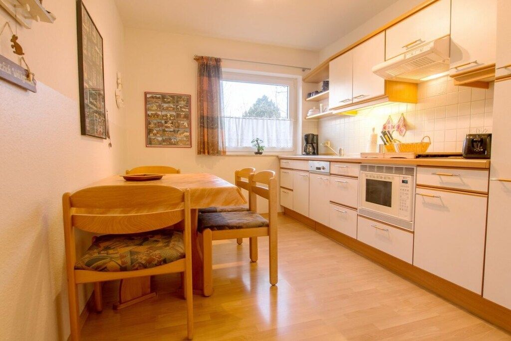 A compact kitchen with a dining table, chairs, a window with curtains, and white cabinetry.