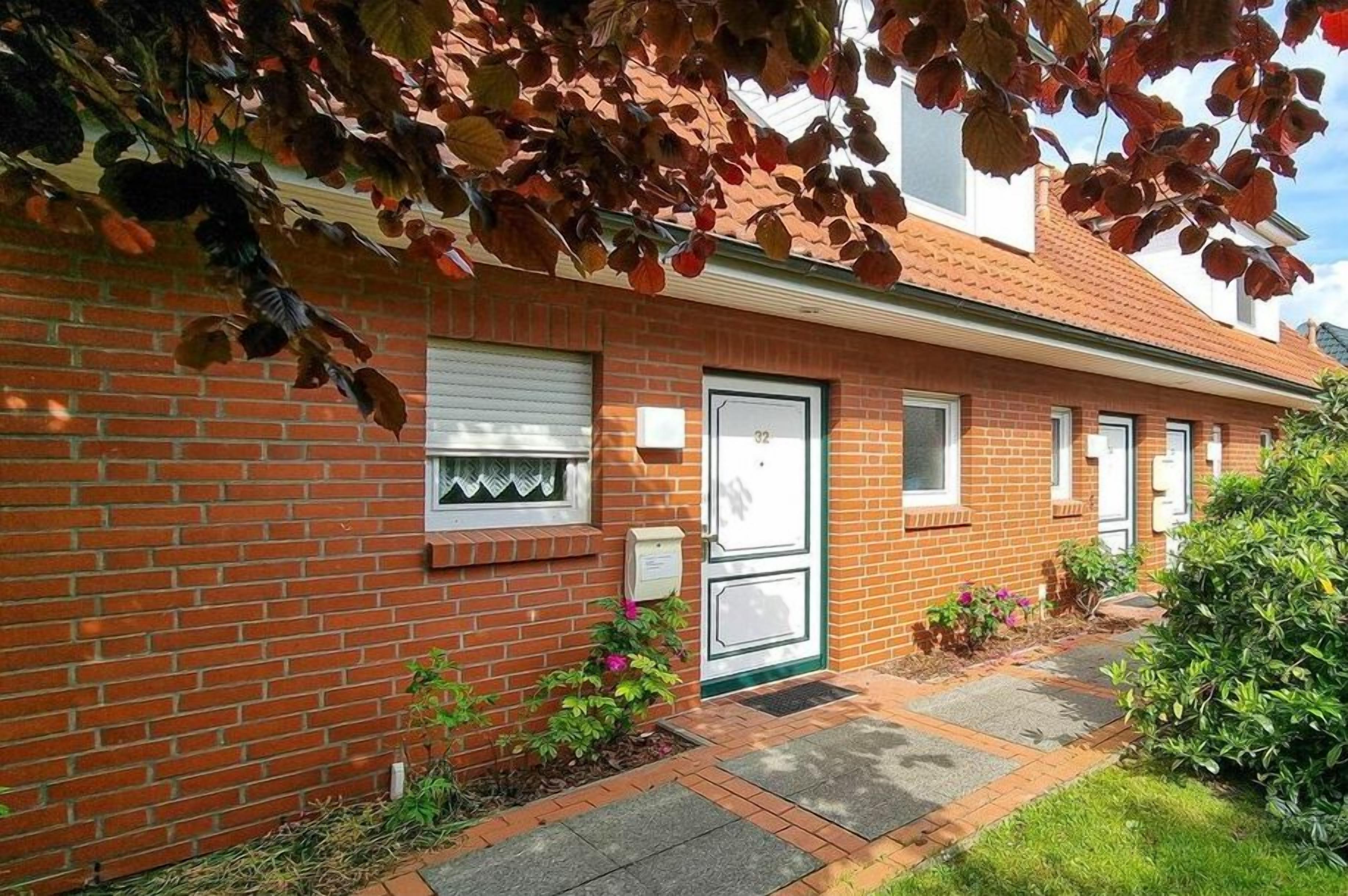 A brick building with a green door, a window with a white frame, and a small garden area with plants and a pathway.
