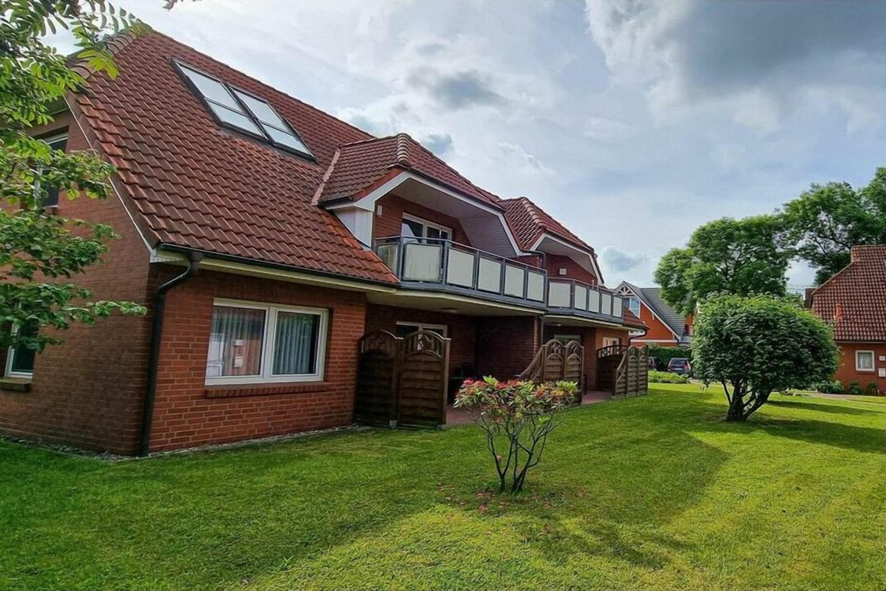 Ein zweistöckiges Haus mit rotem Ziegeldach, einer Veranda und einem kleinen Garten.