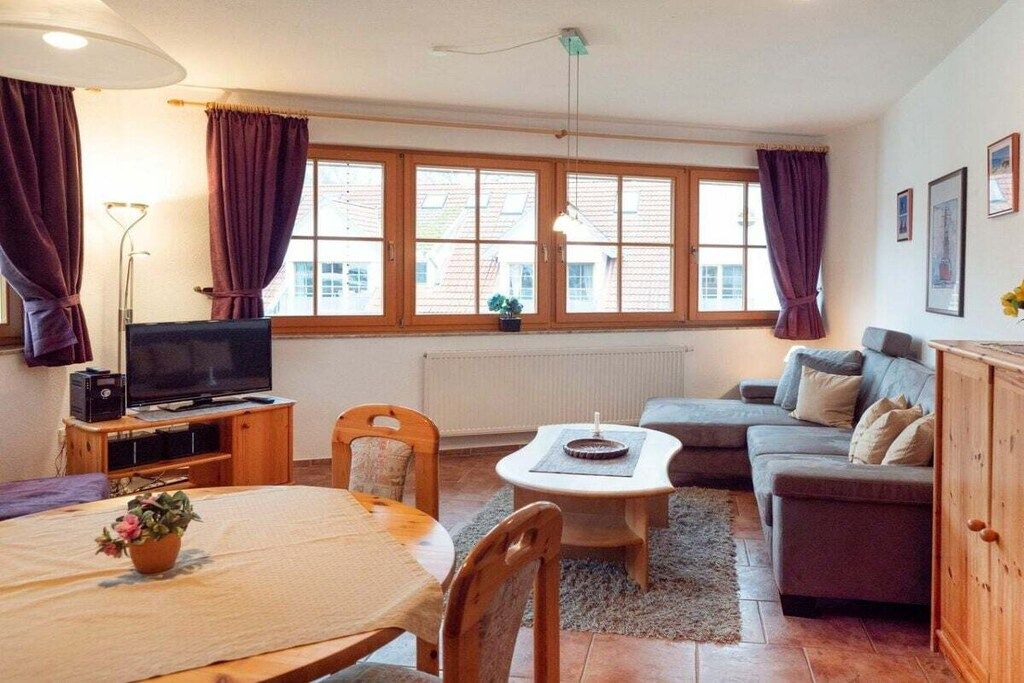 A furnished living room with a television, sofa, dining table, and chairs.