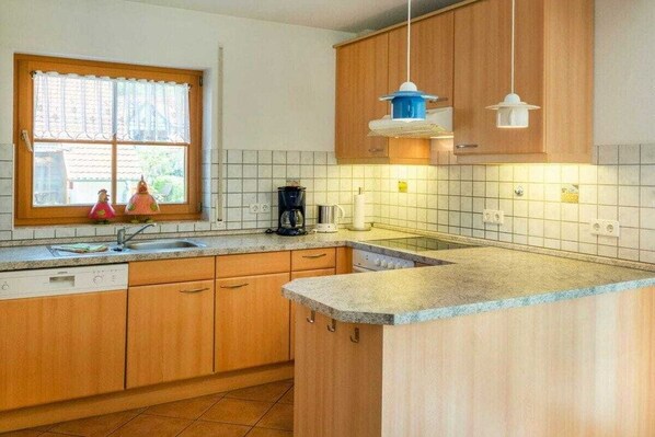 A kitchen with wooden cabinets, a window with curtains, a sink, and a coffee maker. - 10/T6 holiday home park “Freesenbruch” (Zingst (Ostseeheilbad))
