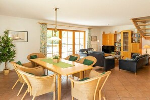 A furnished living room with a dining area, a sofa, a TV, and a bookshelf. - 10/T6 holiday home park “Freesenbruch” (Zingst (Ostseeheilbad))