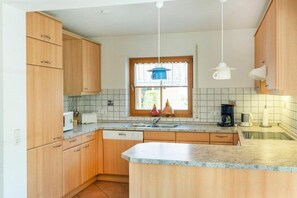 Une cuisine avec des meubles en bois, un plan de travail en granit, une fenêtre avec un rideau et un luminaire suspendu.