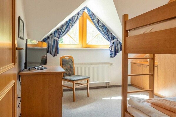 Quarto com beliche, escrivaninha com computador, cadeira e janela com cortinas.