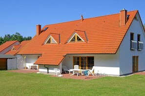 Une maison à deux étages avec un toit en pente, une terrasse couverte aménagée avec du mobilier d’extérieur et un garage.