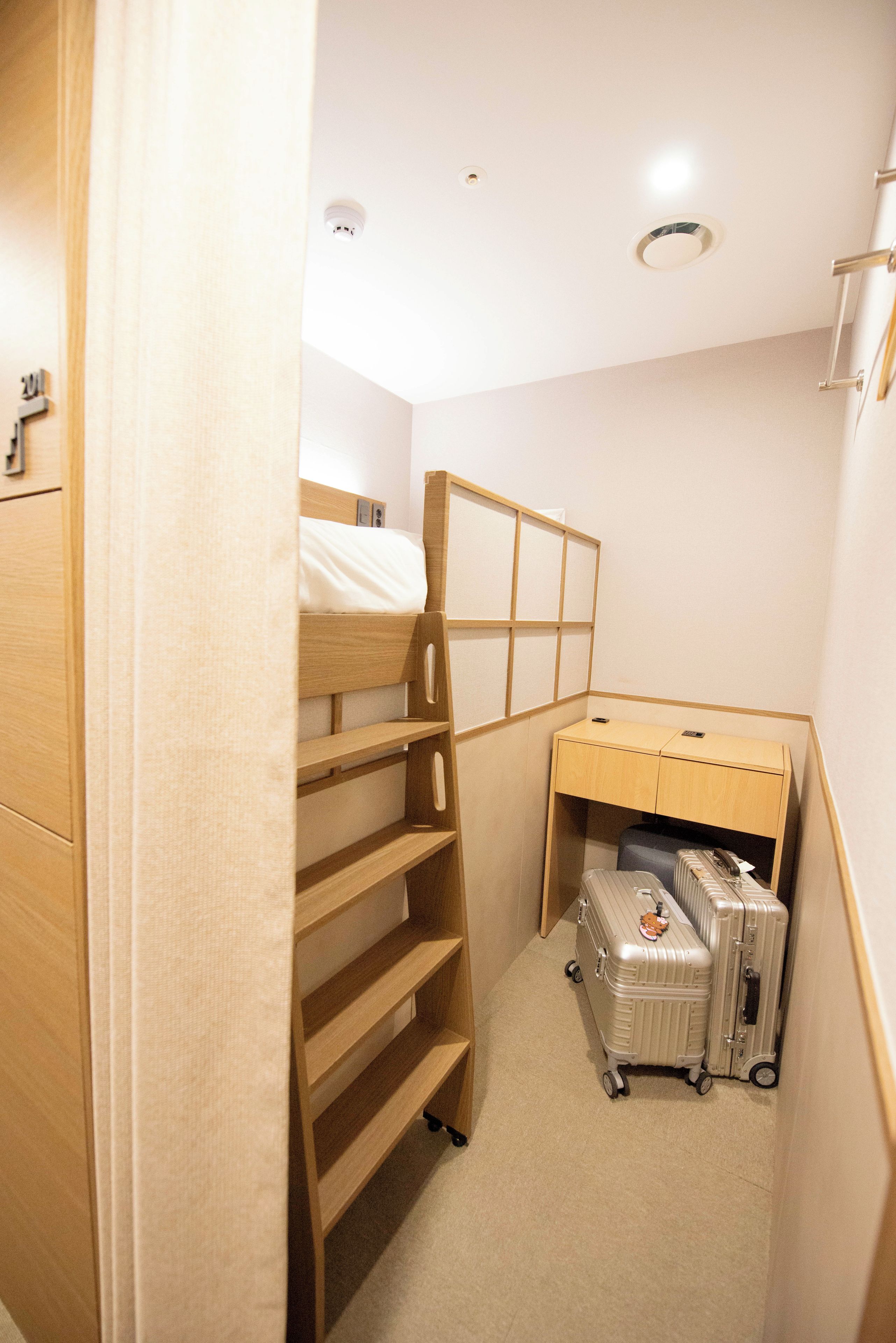 A small, compact room with a bunk bed, a desk with a chair, and a suitcase.