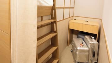 A small, compact room with a bunk bed, a desk with a chair, and a suitcase.