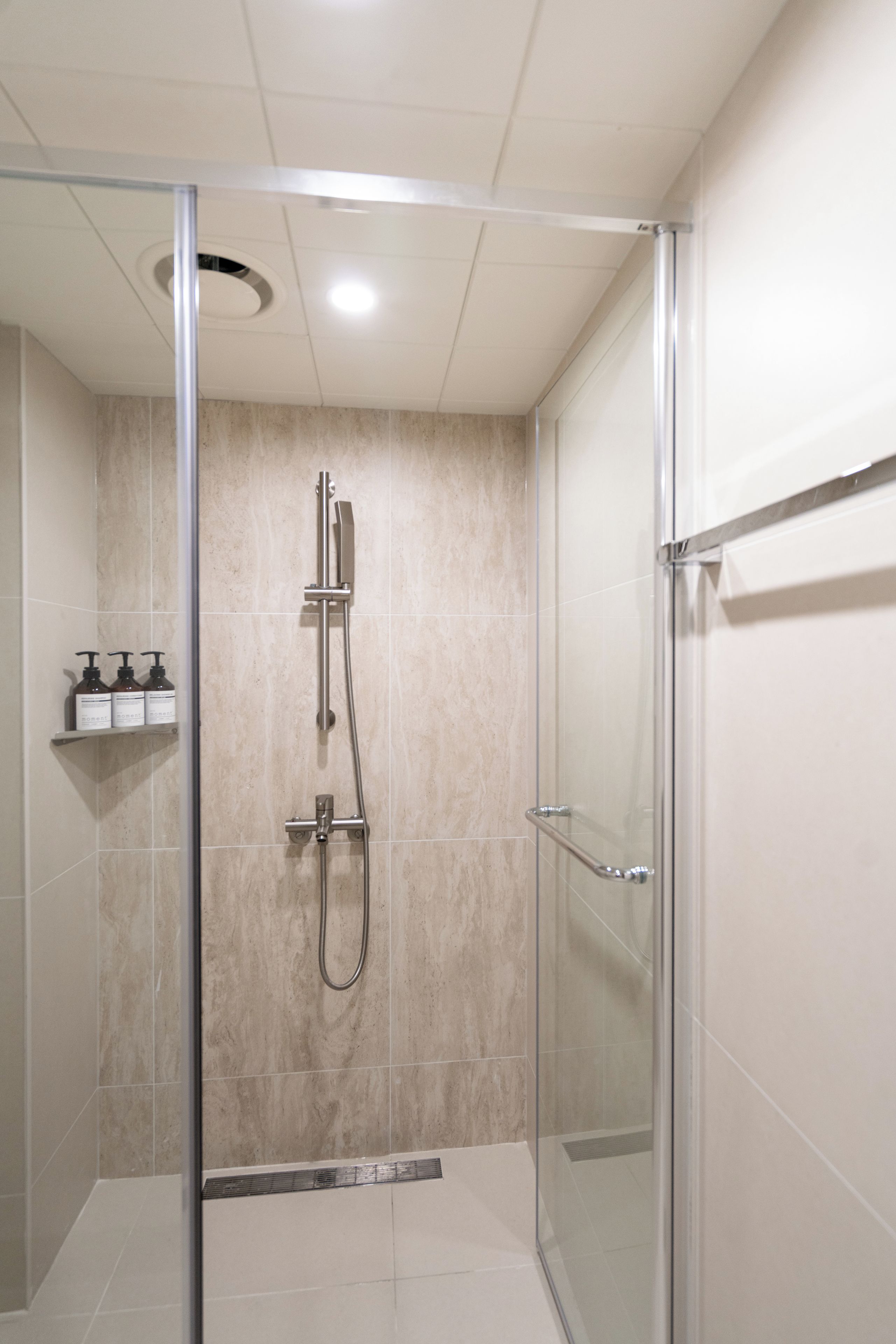 A glass-enclosed shower stall with a handheld showerhead and a wall-mounted faucet.