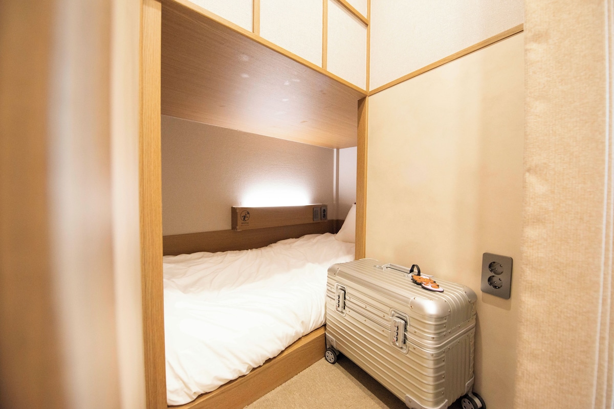 A compact room with a single bed, a suitcase, and a small bedside table.