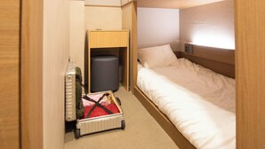 Ett kompakt hotellrum med en våningssäng, en resväska och ett litet skrivbord med en stol.