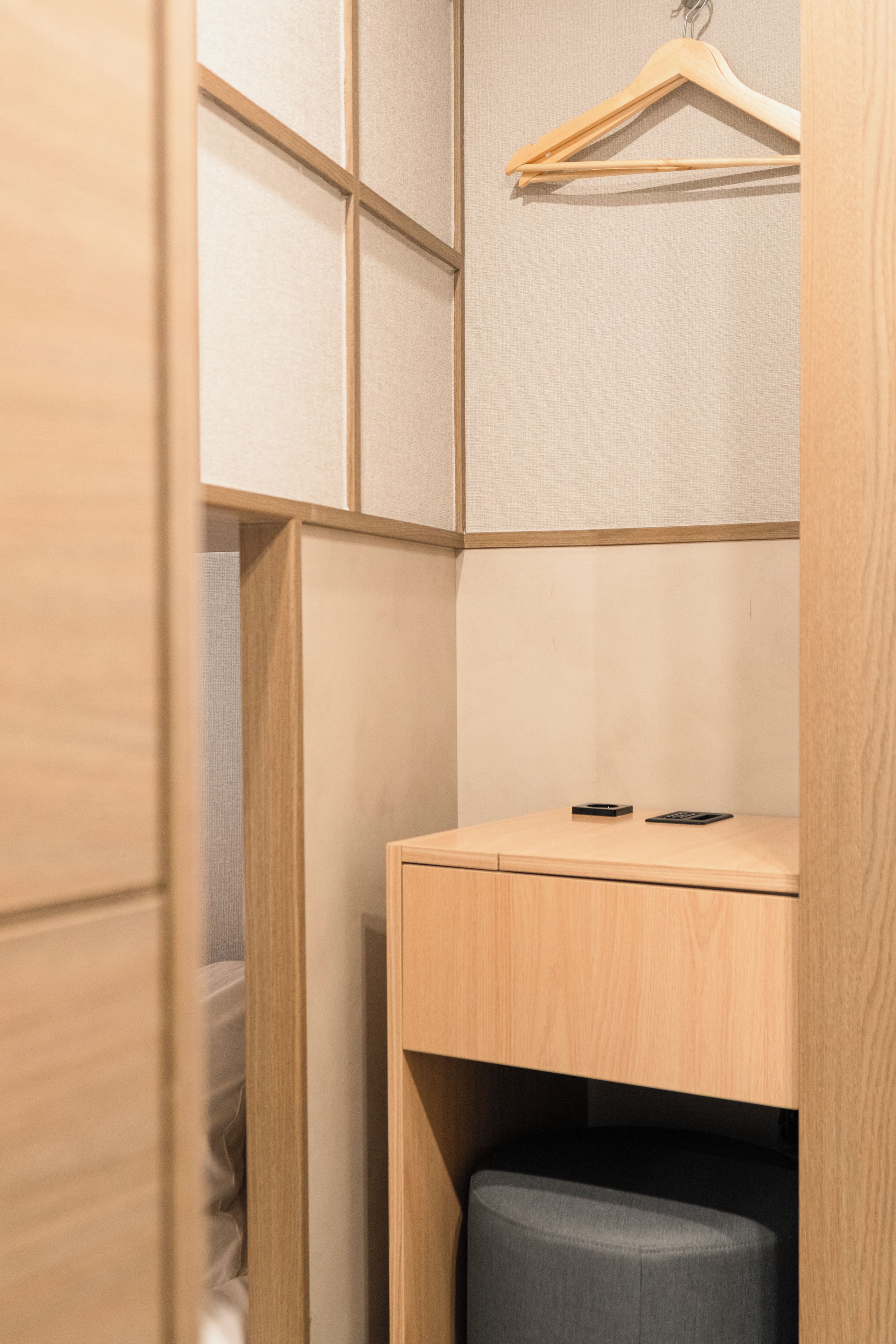 A corner of a room with a wooden wardrobe, a hanging clothes rack, and a small table with a black object on it.