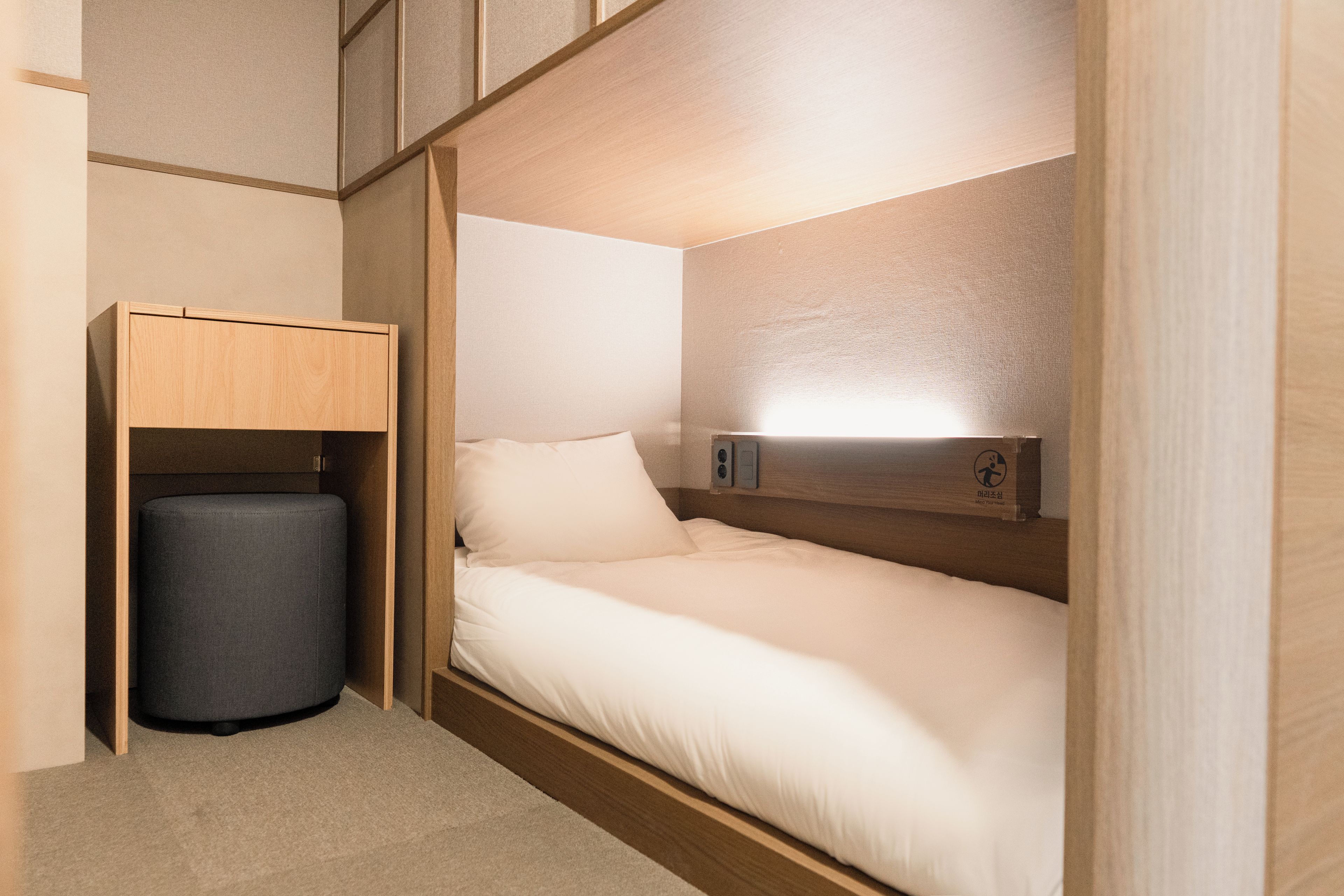 A compact room with a single bed, a small bedside table, and a wall-mounted light.