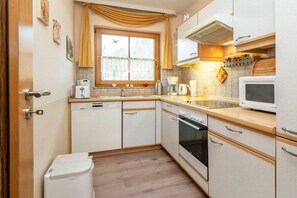 A compact kitchen with a dishwasher, oven, microwave, and a window with curtains. - 4.1/T4 holiday home park “Freesenbruch” (Zingst (Ostseeheilbad))