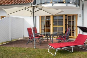 An outdoor patio with a table and chairs, a sun umbrella, and a red lounge chair. - 4.1/T4 holiday home park “Freesenbruch” (Zingst (Ostseeheilbad))