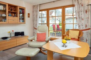 A room with a dining table, a chair, a cabinet with books, and a window with curtains. - 4.1/T4 holiday home park “Freesenbruch” (Zingst (Ostseeheilbad))
